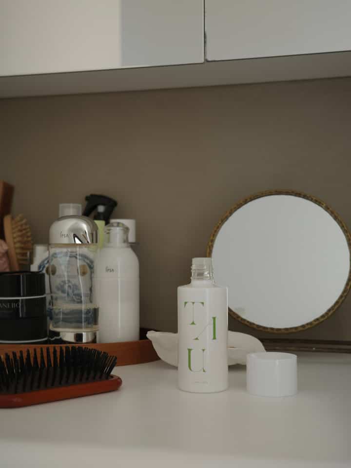 ベージュの壁と白い化粧台が配置されたパウダールーム、鏡とヘアオイル、ブラシが置かれたシンプルな空間