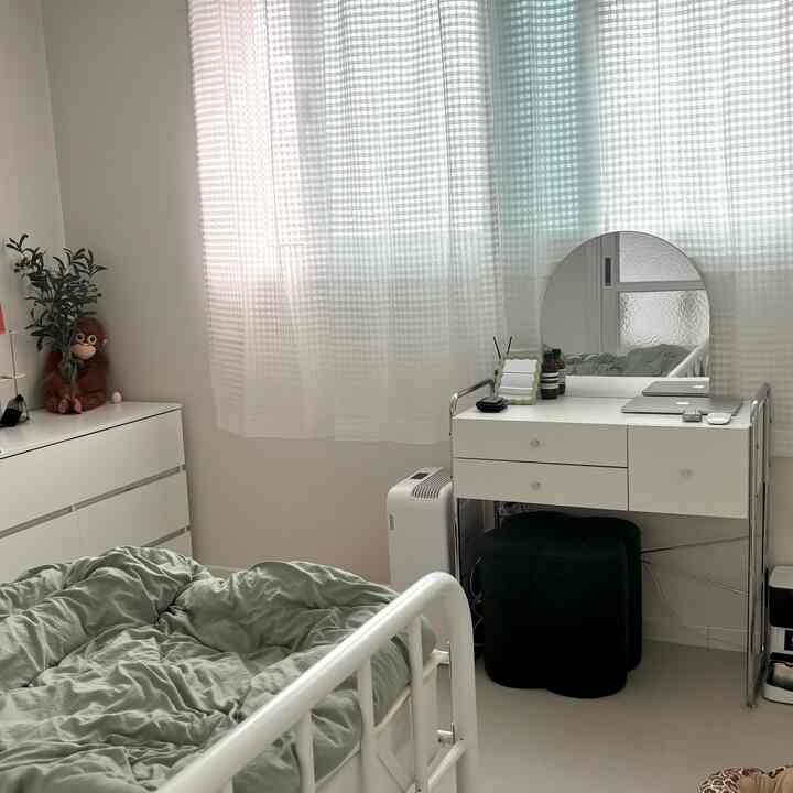 柔らかなホワイトトーンの寝室にミッドセンチュリーモダンの化粧台と黒いスツールが配置された印象的な狭い空間