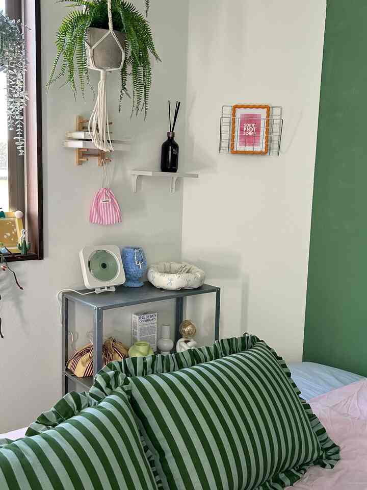 白と緑の壁が調和した寝室、緑のストライプクッションと寝具がアクセントの落ち着いた雰囲気のインテリア