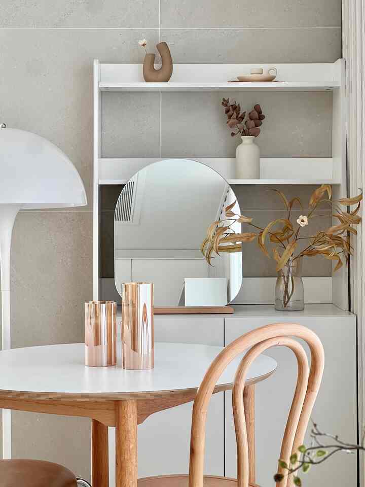 ホワイトとブラウンのナチュラルトーンのダイニングルーム、丸いダイニングテーブルと木製の椅子、鏡とオブジェが調和したミニマルで印象的な空間