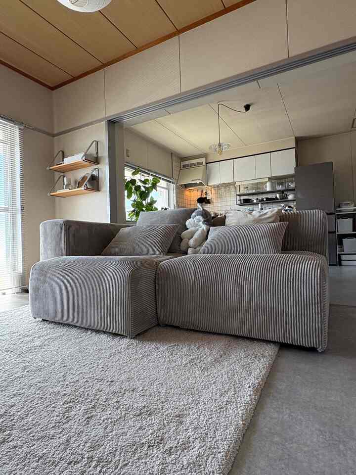 Beige natural-toned living room connected to kitchen featuring a central corduroy sectional sofa and light-colored rug with cozy atmosphere