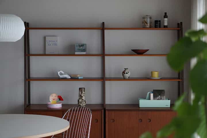 A dining room with white walls and wood tone furniture, featuring vintage-style shelves and a round table creating a natural ambiance
