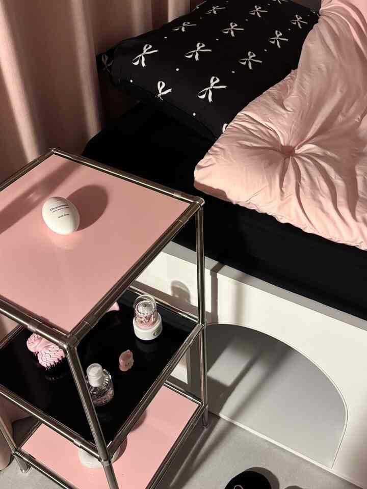 ピンクと黒の色調の寝室、ピンクのメタルシェルフと黒いベッドが配置された雰囲気のある空間