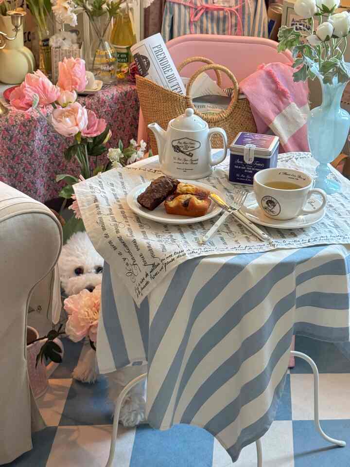 パステルピンクとブルーの落ち着いたカフェ風空間、花とテーブルセットが配置されたナチュラルなインテリア