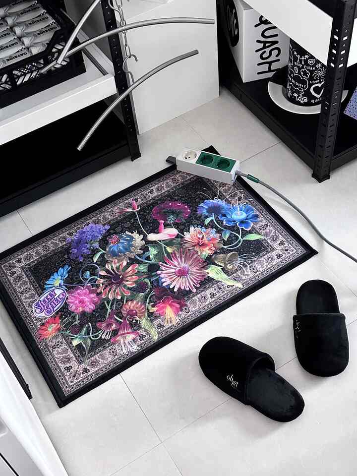 Monotone entrance featuring black floral door mat and black slippers on white tiled floor