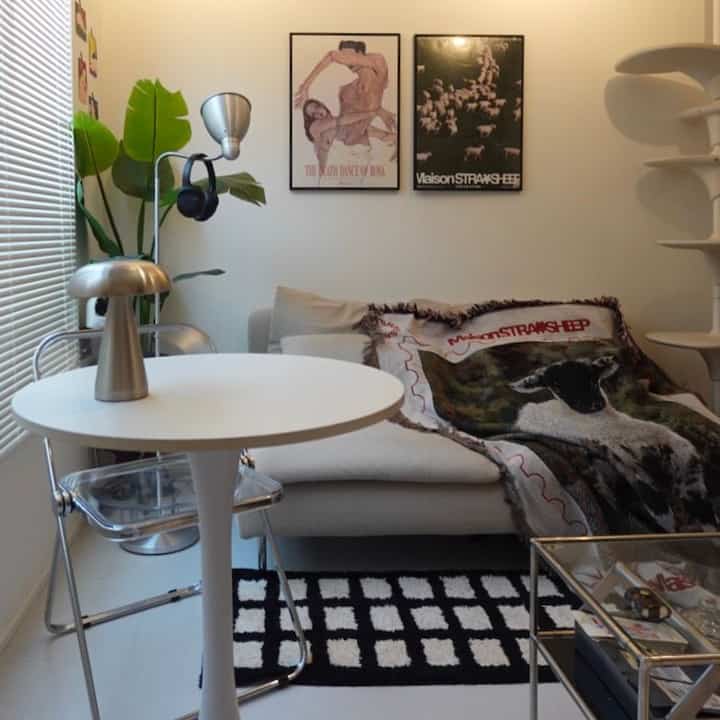 白と黒のトーンのリビング、セクショナルソファと猫柄のブランケット、ブラインドと植物が配置されたナチュラルモダンなインテリア