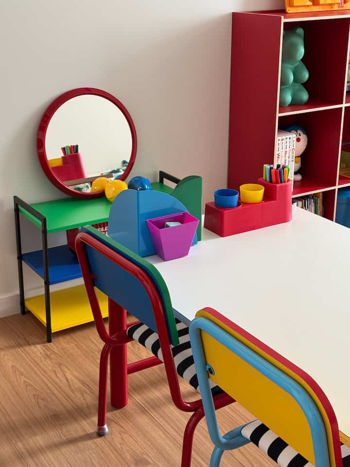 赤・青・黄のカラフルな子供部屋、白い机と色とりどりの椅子、多彩な棚が配置された雰囲気のあるインテリア