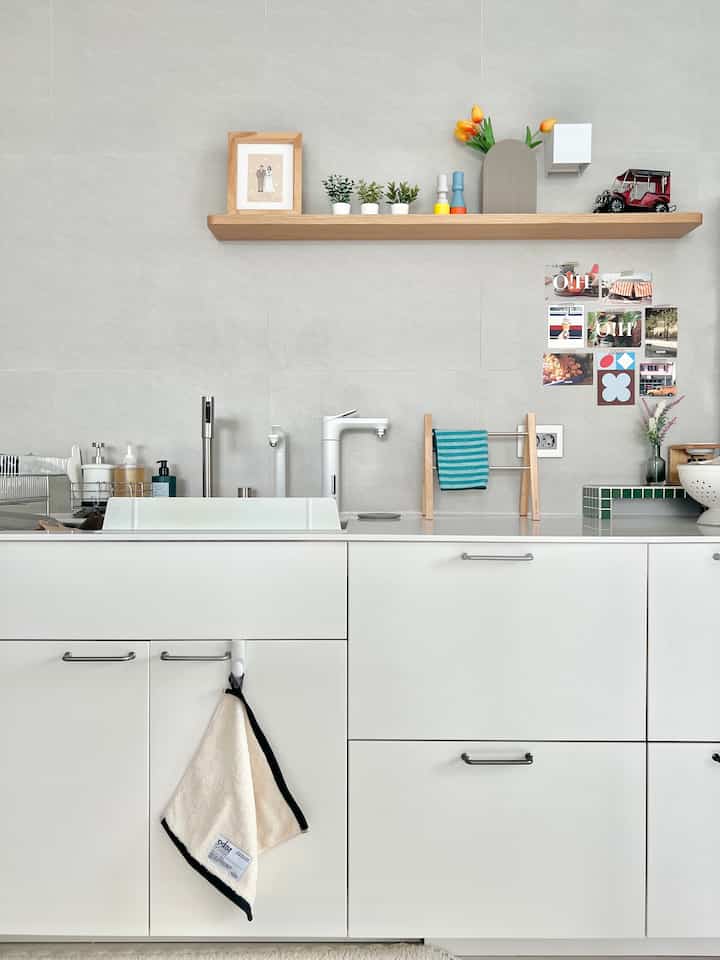 White and natural toned kitchen featuring a wood shelf with plants and kitchen towels, giving a clean and cozy atmosphere