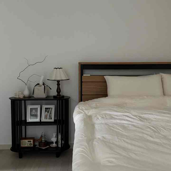 White-walled bedroom featuring wood-tone bed frame and black console table with natural décor