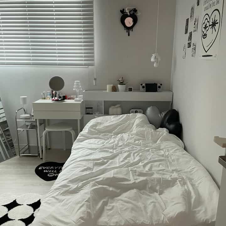 Simple monotone bedroom in white and black, featuring a single bed, dresser, and blinds in a tidy arrangement