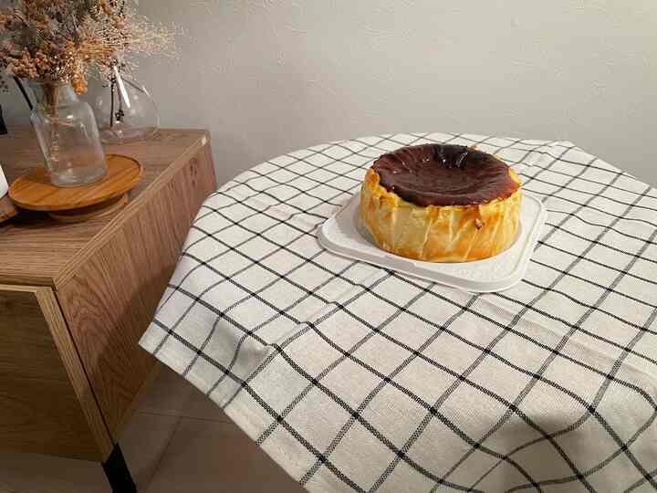 白いチェック柄のテーブルクロスが敷かれたダイニングテーブルにバスクチーズケーキが置かれた北欧風の温かみのあるインテリア