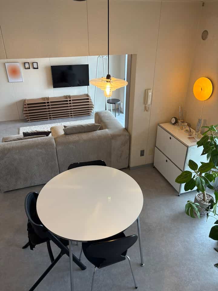 Simple interior space with white and black toned living room and dining table, featuring greenery from a leafy plant for natural ambiance