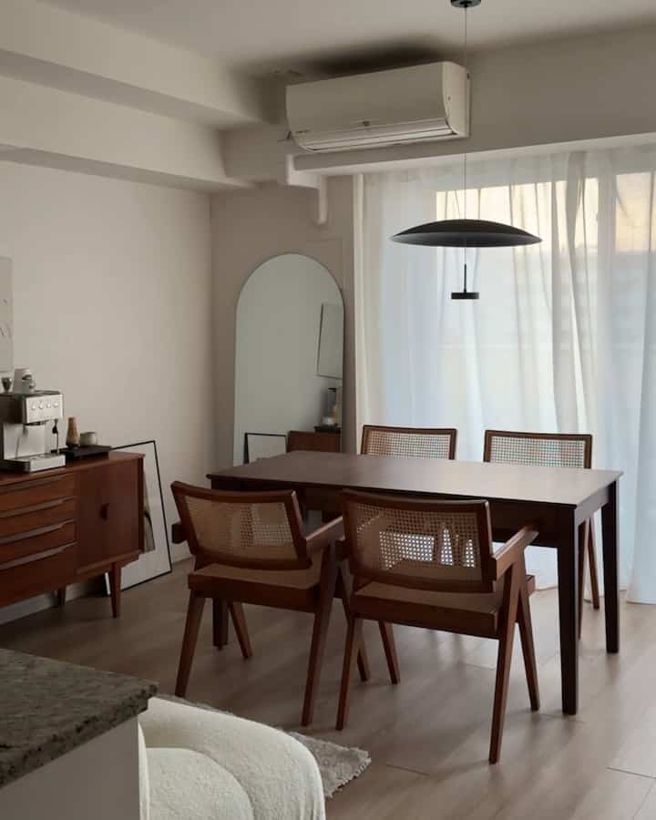 明るいホワイトの壁と木目調の家具が配置されたモダンなナチュラルダイニング、中央にエクステンション可能なブラウンのダイニングテーブルとラタンチェアがある印象的な空間