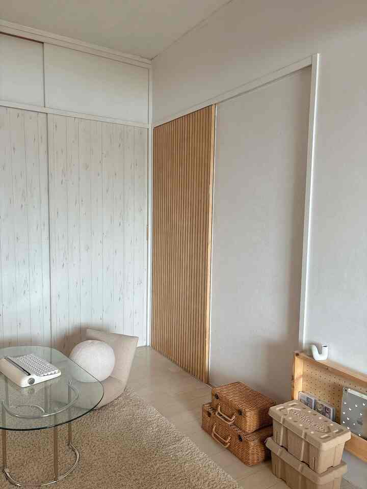 Natural-toned kids' room featuring a transparent glass table and wooden sliding doors, creating a simple and cozy atmosphere