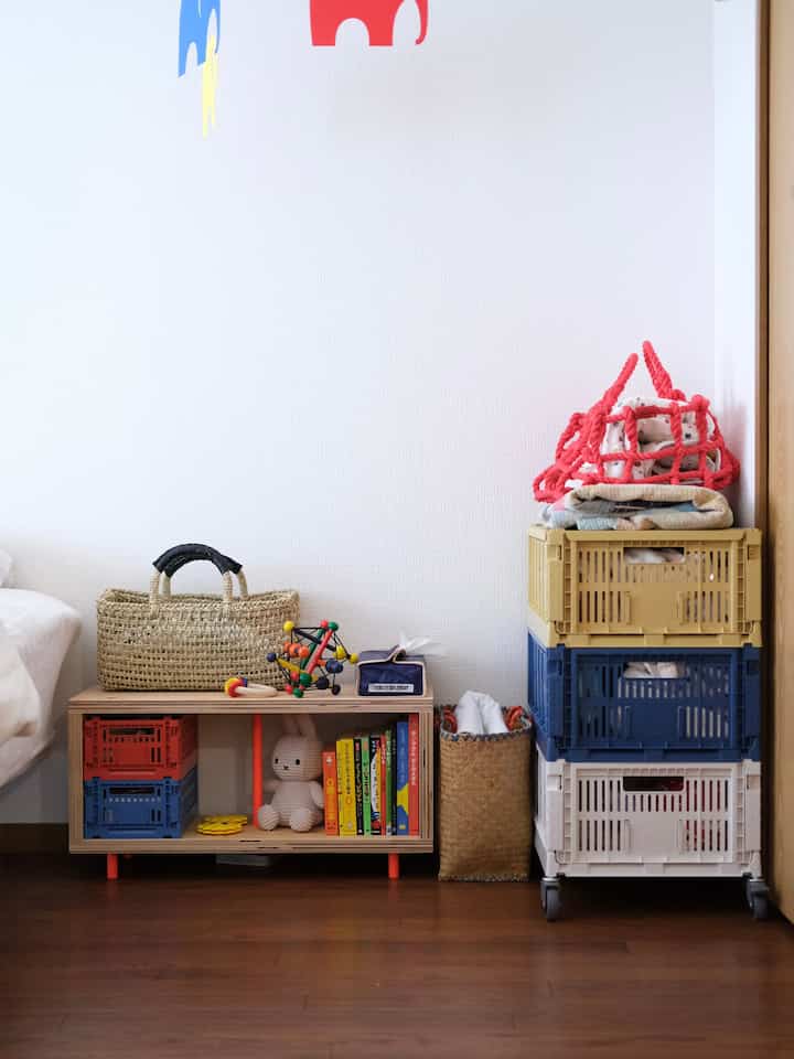白い壁とナチュラルな木目調の棚がある子供部屋、オレンジのポイントカラーが効いた収納スペースと整理された絵本やおもちゃのある雰囲気のあるインテリア