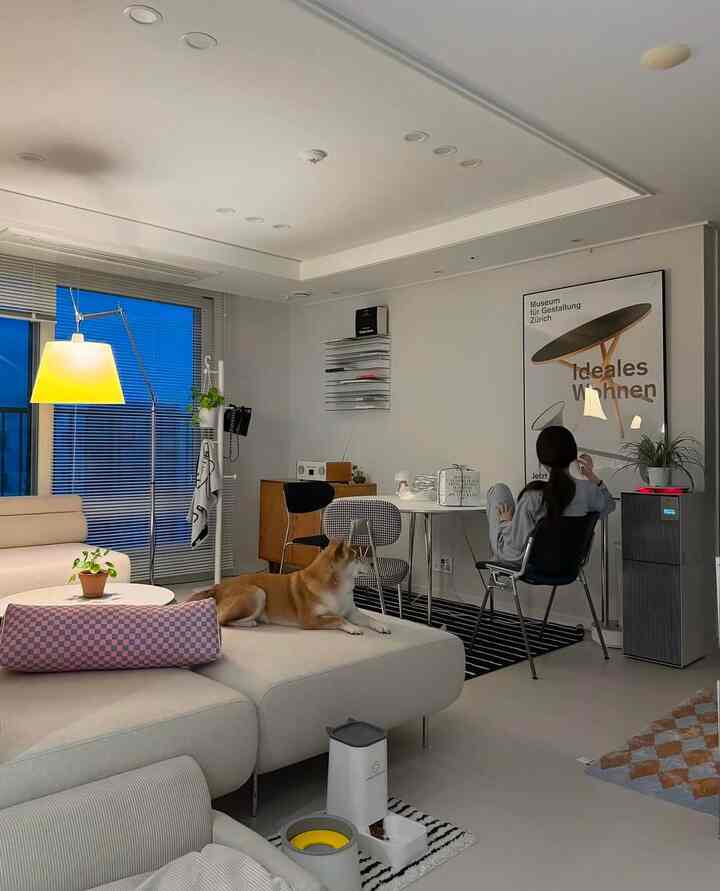 ナチュラルトーンのモダンなリビング、ベージュのソファと犬、黄色いフロアランプが配置された落ち着いた空間