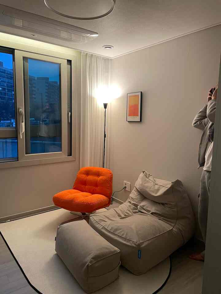 A white-toned small living room featuring a beige bean bag and orange armchair with a cozy natural atmosphere