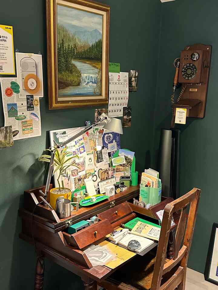 ダークグリーンの壁とヴィンテージの木製デスク、壁掛け電話が配置された落ち着いた書斎空間