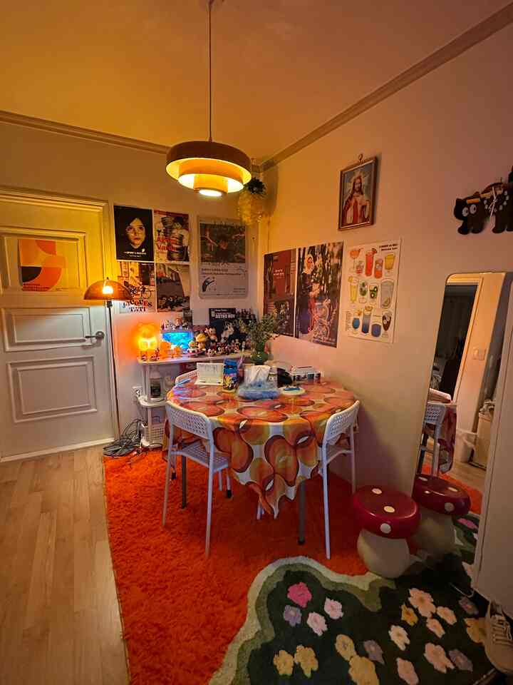 オレンジ色調のダイニングルーム、丸テーブルと白い椅子、多様なポスターと個性的なキノコスツールが配置された温かみのある空間