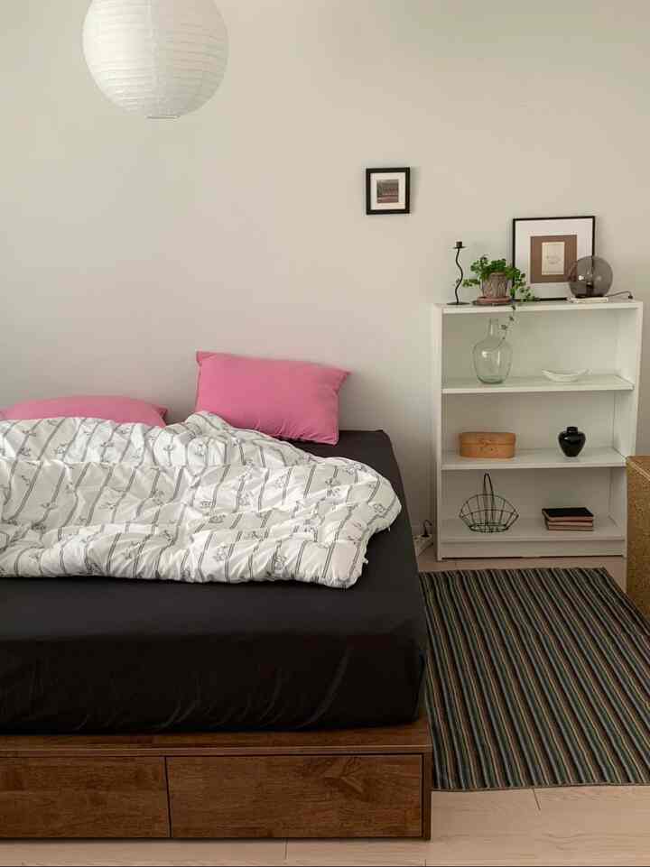 ホワイトとナチュラルカラーが基調の寝室、ピンクの枕と模様入り布団が配置されたシンプルなインテリア空間