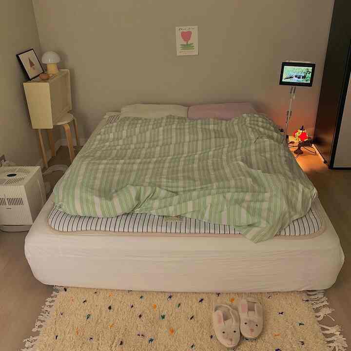 ナチュラルなベージュ色調の寝室、中央にストライプ柄の掛け布団と枕を配したベッドと、ラグの上に置かれたウサギのルームシューズが印象的な温かみのあるインテリア