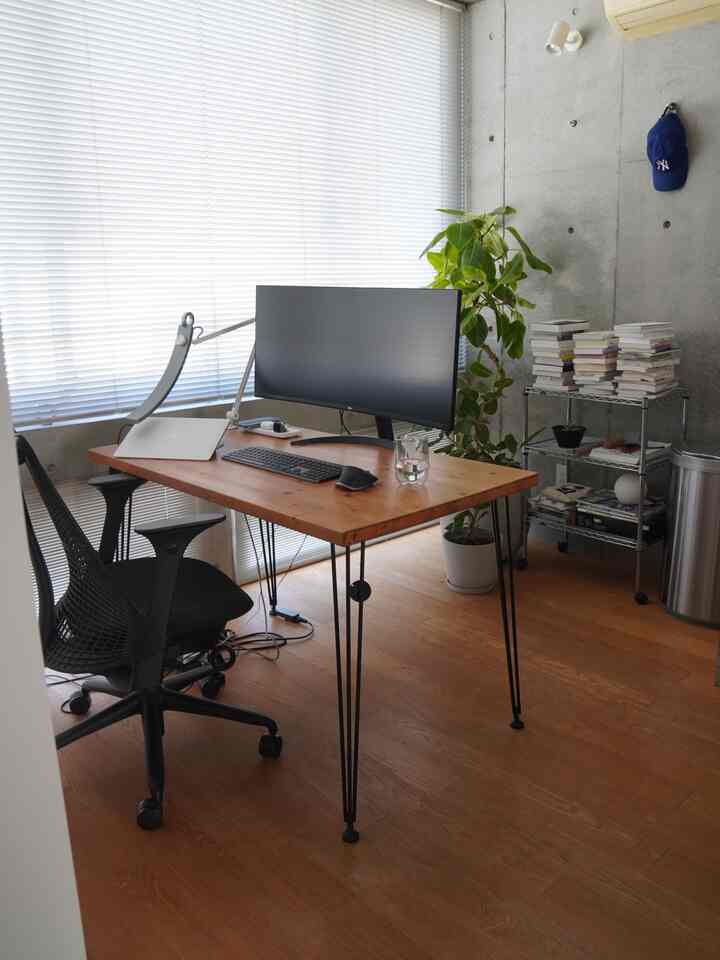 明るい自然光とグレーコンクリート壁のシンプルでモダンなホームオフィス、木製デスクと黒いオフィスチェアを配した雰囲気のあるインテリア