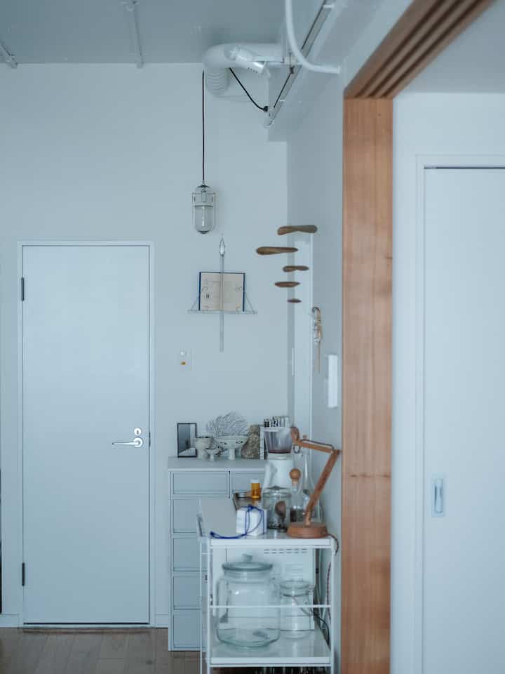 白を基調とした玄関の空間、木目調の扉枠と収納キャビネット、壁面照明が配置されたミニマルなインテリア