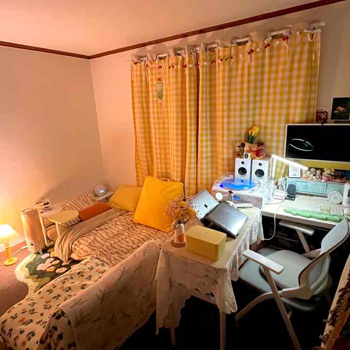 黄色のチェックカーテンと白い壁のワンルーム、黄色のクッションとコンパクトなホームオフィスが配置された雰囲気のあるインテリア