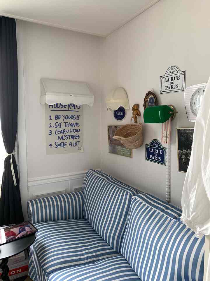 白い壁と青のストライプソファが配された居心地の良いリビングの一角、フレンチ風壁飾りとカフェ風の雰囲気のあるインテリア