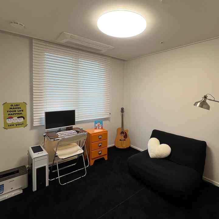 白い壁と黒いカーペットのコンパクトなホームオフィス、オレンジ色の引き出しとギターが配置された雰囲気のある空間