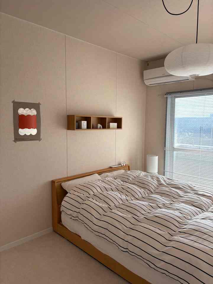 ナチュラルな木目調とホワイトの寝室、ストライプの掛け布団カバーと壁掛け棚が配置されたホテルライクな雰囲気のインテリア