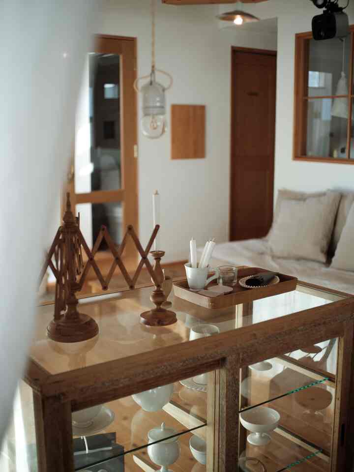 木目調と白を基調としたアンティーク風リビング、ガラス天板のキャビネットにキャンドルや小物が置かれた印象的な空間