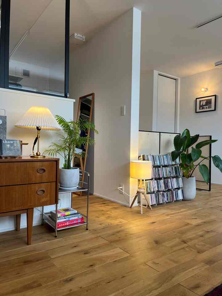 Wood tone floor and white walls blend in living room featuring vintage nightstand, table lamps, and various plants creating a cozy atmosphere
