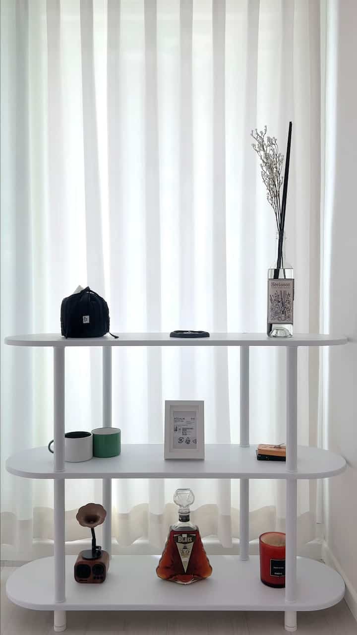 Clean and modern living room featuring a white-toned shelf with various objets and white curtains blending harmoniously