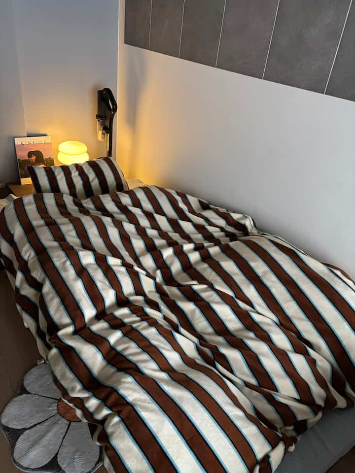 Ivory and brown striped bedspread in a compact studio bedroom with a cozy and natural atmosphere