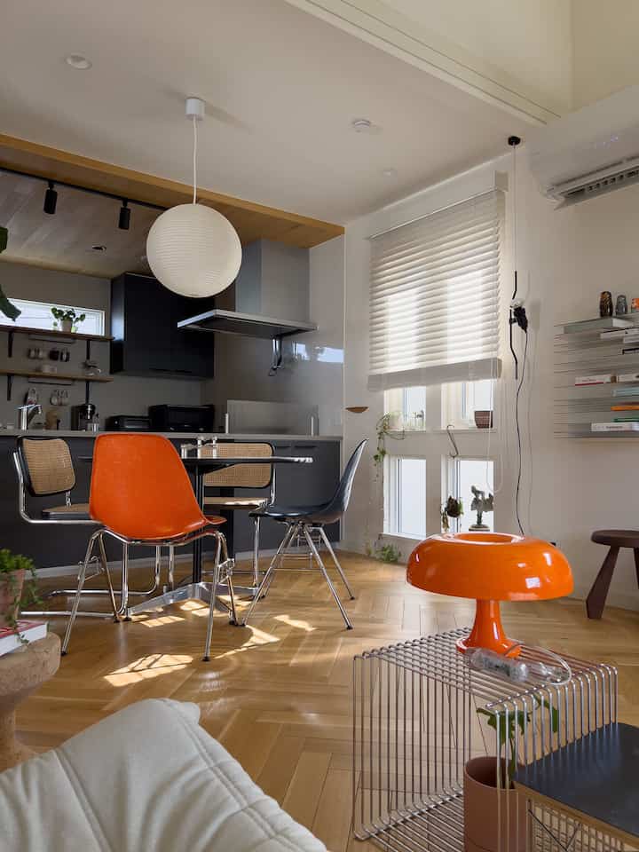 木目調の床と白い壁が調和したモダンなダイニング、鮮やかなオレンジの椅子と照明が印象的な空間