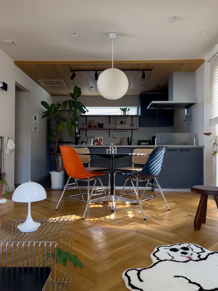 Modern dining room with warm wood-tone floor and ceiling, orange and navy stools around dining table, dog-shaped rug creating cozy feel