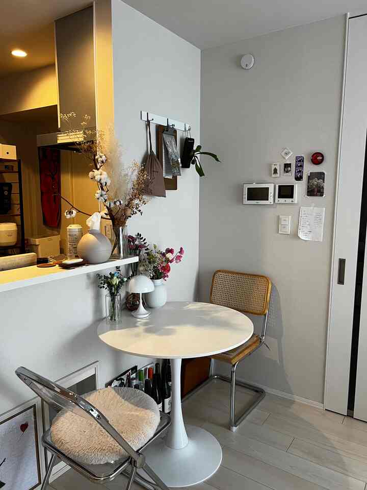 白を基調としたコンパクトなダイニングスペース、丸テーブルとラタンチェア、花瓶とテーブルランプが置かれた雰囲気のあるインテリア