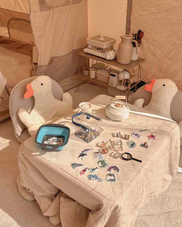 ベージュ色調のコンパクトなホームキャンピング空間、子供用チェア2脚とテーブルの上のベビー用おもちゃが配置された居心地の良い室内テント