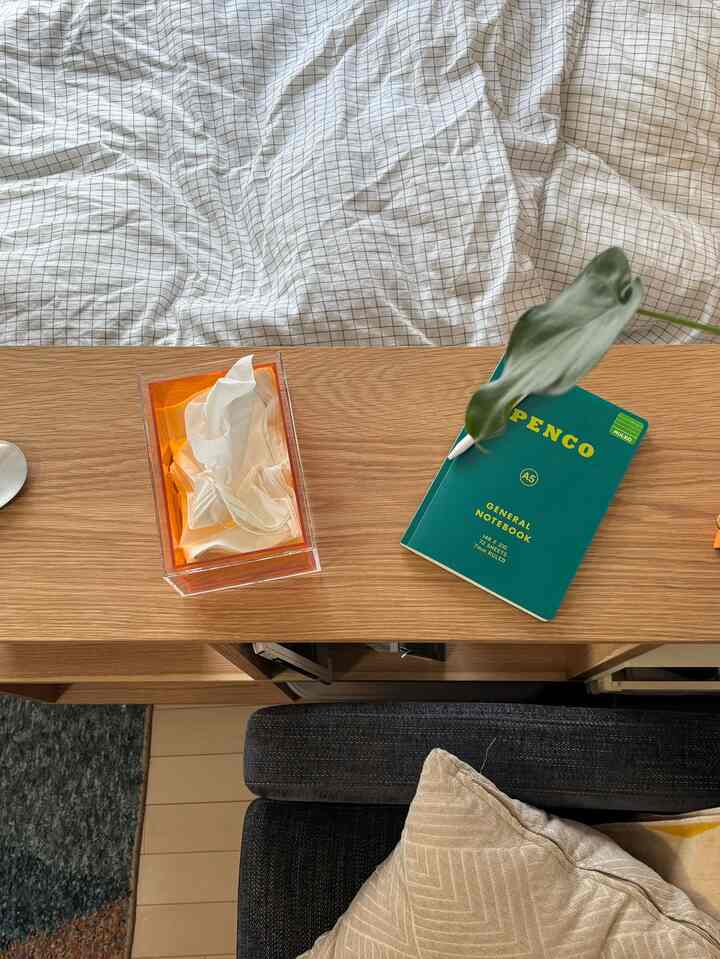 木目調のデスクにアクリル製ティッシュボックスと緑のノートが置かれた清潔感のあるリビング