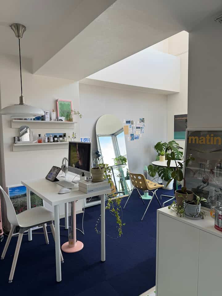 ネイビーカーペットと白い壁のワンルームのホームオフィス、白いデスクとチェア、ペンダントライトが配置された清潔感のある作業空間