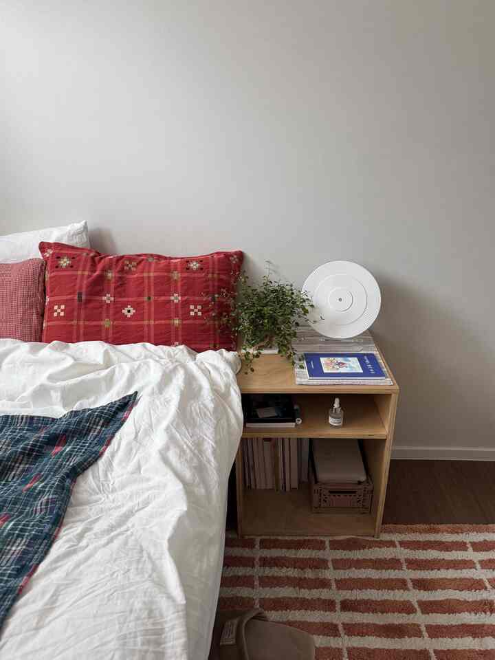 White and natural-toned bedroom featuring a wooden nightstand and green plant creating a calm atmosphere