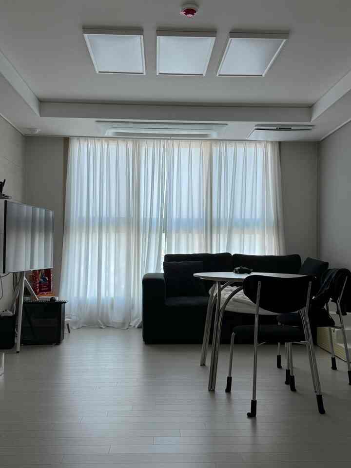 ホワイトとブラックのトーンのモダンなリビング、窓際に置かれたソファと中央に配置された丸テーブルがある清潔感のある空間