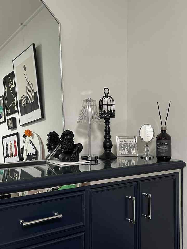 ネイビーのキャビネットの上に様々な額縁とオブジェが置かれた温かみのあるインテリア空間