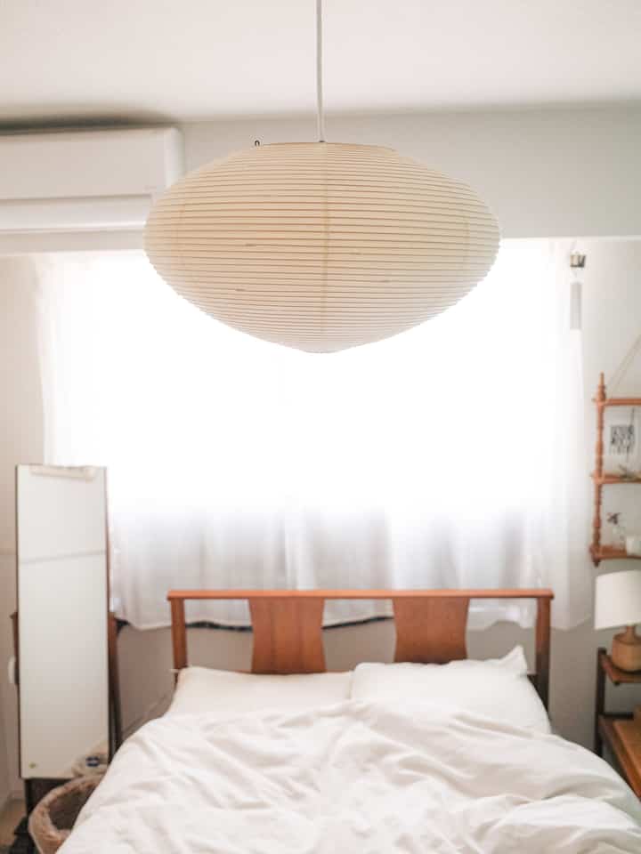 白と茶色を基調とした寝室、イサムノグチのアカリペンダントライトと自然な木製家具が調和するシンプルでナチュラルな雰囲気のインテリア