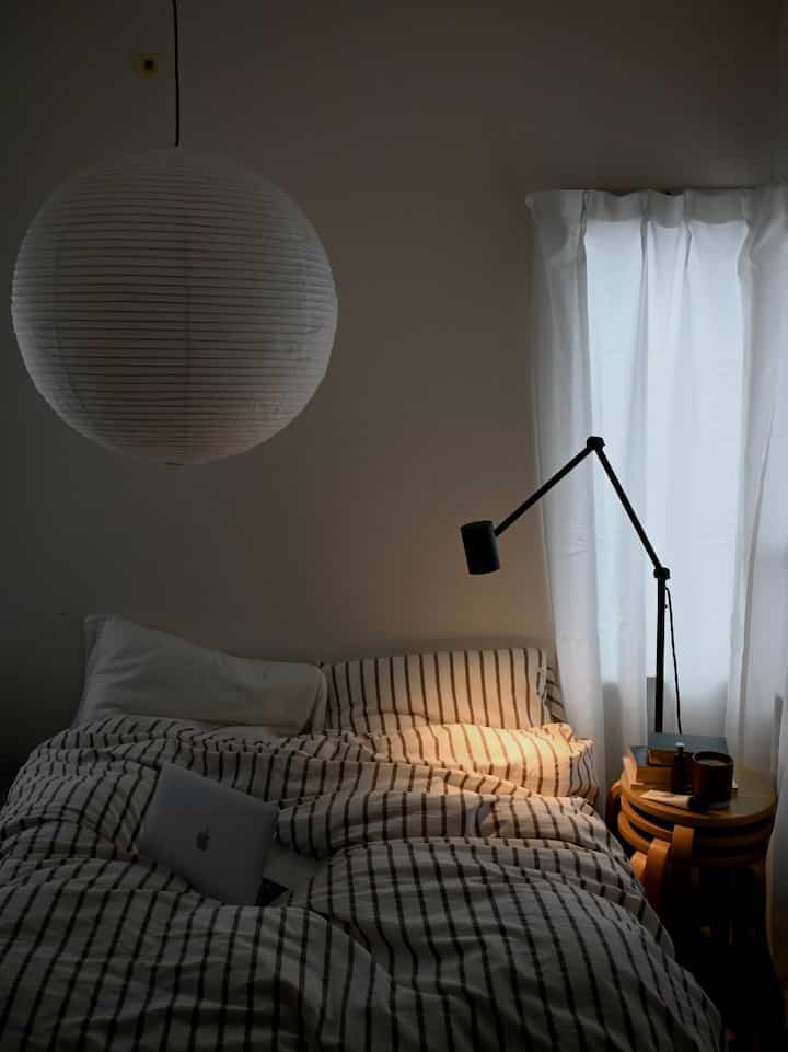 White and brown toned bedroom featuring striped bedding and a standing lamp with cozy atmosphere