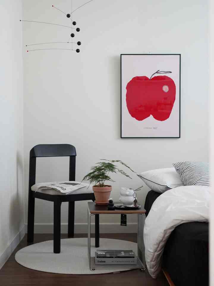 Minimal bedroom with white walls, black furniture, and a red apple poster on the wall