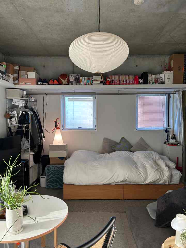 白とナチュラルブラウンのトーンのワンルーム寝室、ベッドとソファ、ペンダントライトが配置された印象的な空間