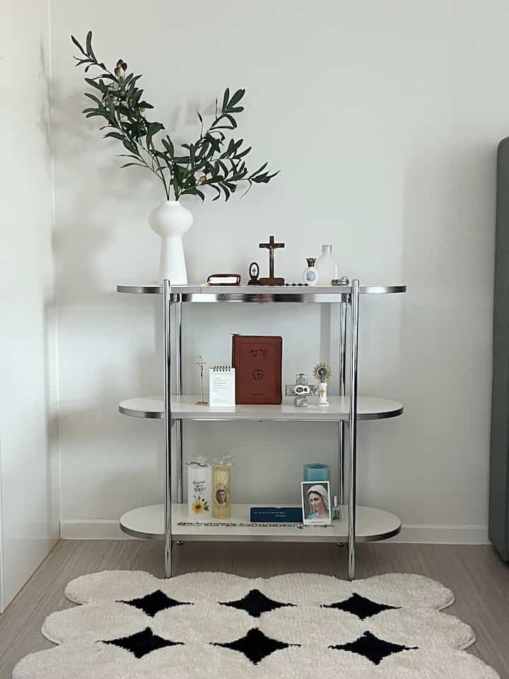 White and green entrance space featuring a simple nightstand shelf with an olive branch artificial plant and religious objets in a neat arrangement