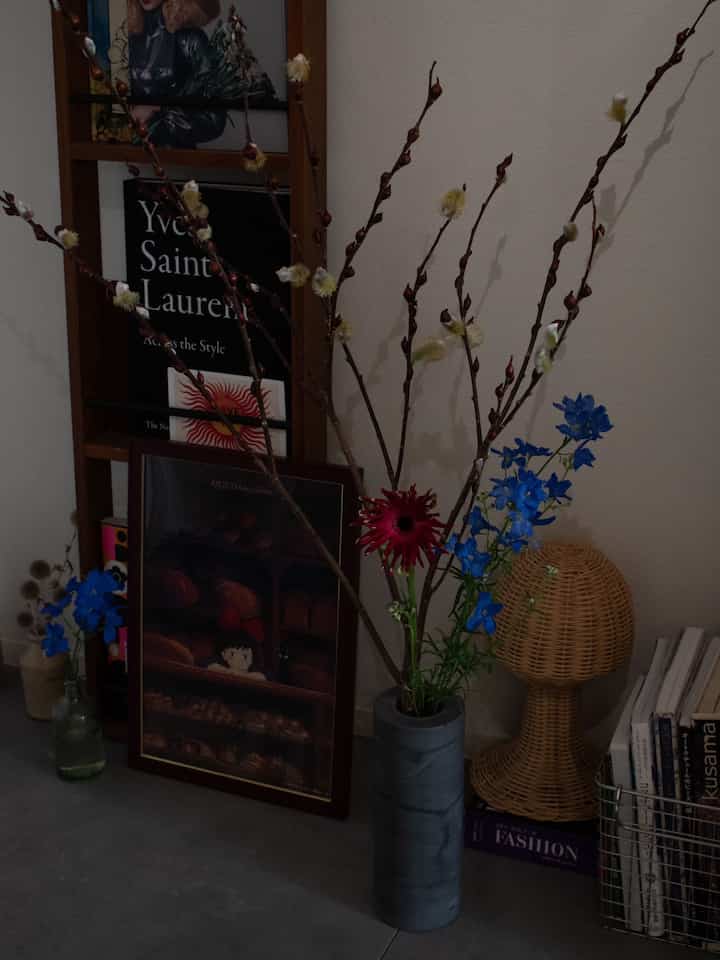 暗い色調の室内空間、壁際に多様な花を飾った花瓶と複数の絵画が配された雰囲気のあるインテリア